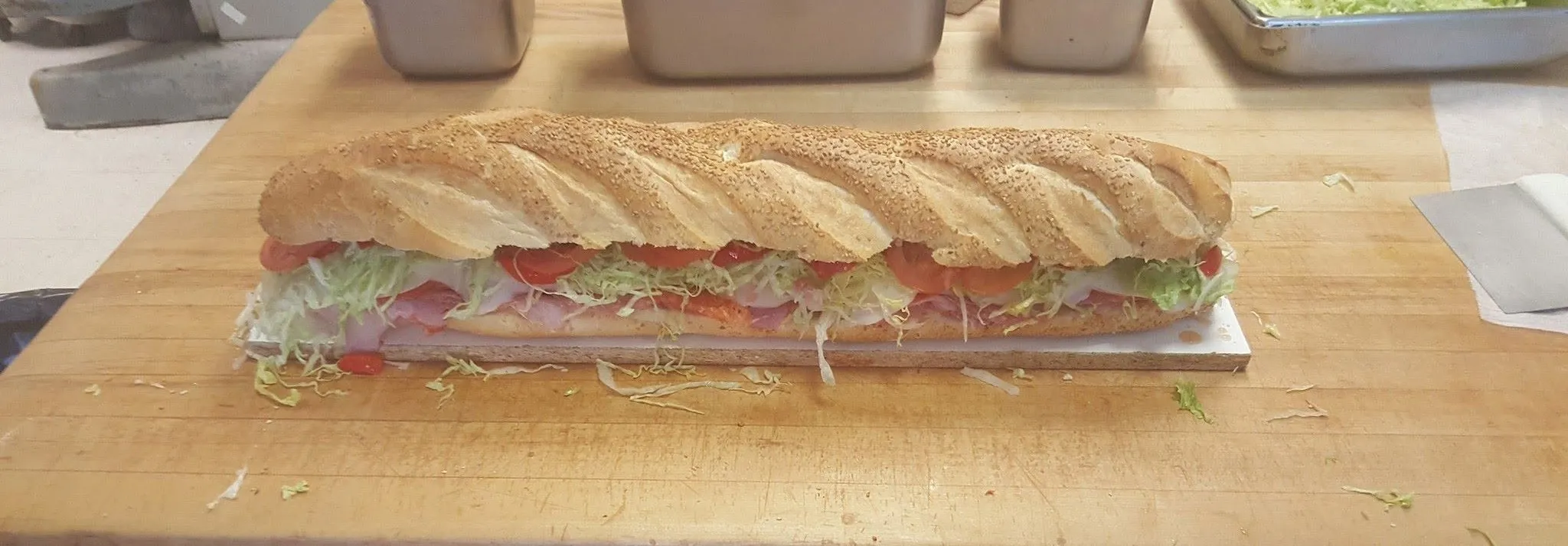 Long Italian hero on a sesame loaf, filled with cold cuts, shredded lettuce and tomato, on a butcher block