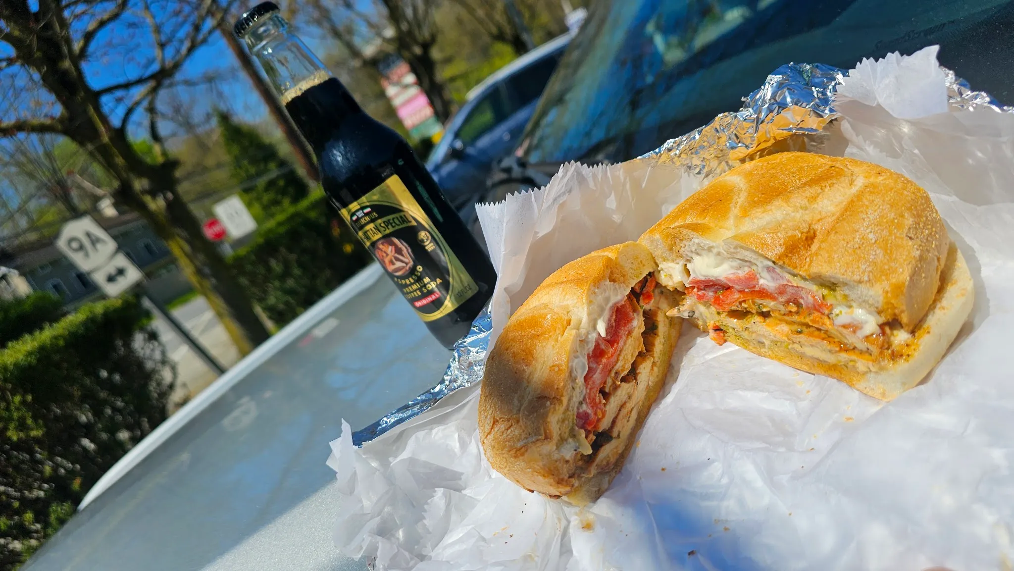 Sandwich cut in half, filled with grilled chicken, roasted red peppers, fresh mozzarella and pesto, next to a bottle of Manhattan Special