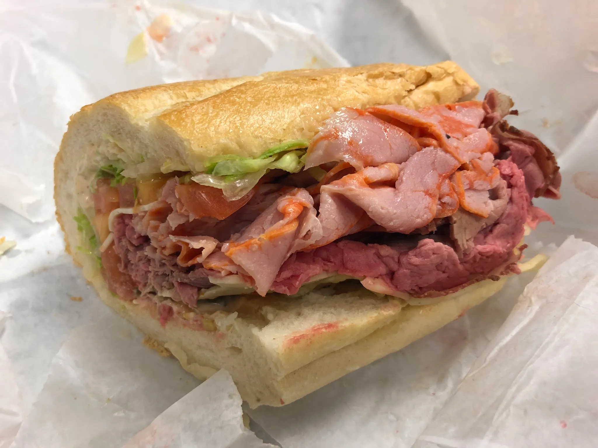 Hero roll stacked with sliced roast beef and ham, lettuce and tomato, on white deli paper